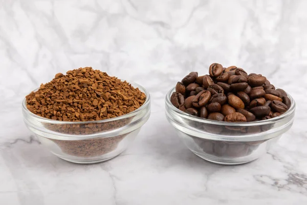 Coffee granules and coffee beans on a white marble background. Instant coffee drink. Energy hot drink. Place for text. Place for copy. Cheerful morning concept.