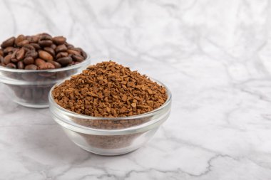 Coffee granules and coffee beans on a white marble background. Instant coffee drink. Energy hot drink. Place for text. Place for copy. Cheerful morning concept.
