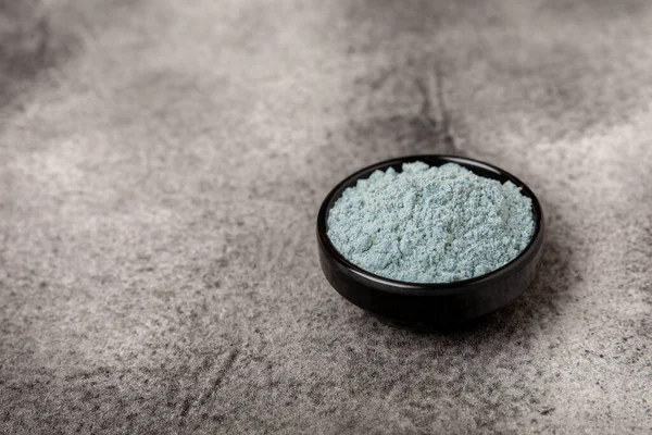 Blue spirulina powder in bowls on black texture background. Natural vegan superfood. Food supplement. Phycocyanin extract. Healthly food. Place for text. Copy space.