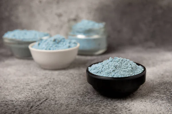 Blue spirulina powder in bowls on black texture background. Natural vegan superfood. Food supplement. Phycocyanin extract. Healthly food. Place for text. Copy space.