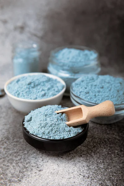 Blue spirulina powder in bowls on black texture background. Natural vegan superfood. Food supplement. Phycocyanin extract. Healthly food. Place for text. Copy space.