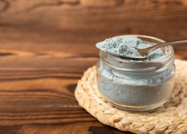 Blue spirulina powder in a glass jar on a brown background. Natural superfood, vegan, healthy food supplement. Phycocyanin extract. Antioxidant. Place for text. Copy space.