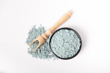 Blue spirulina powder in bowl and wooden spoon isolated on white background.