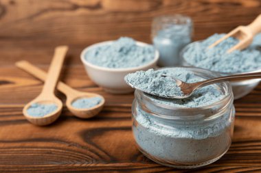 Blue spirulina powder in a glass jar on a brown background. Natural superfood, vegan, healthy food supplement. Phycocyanin extract. Antioxidant. Place for text. Copy space.