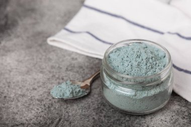 Blue spirulina powder in a glass jar on a black texture background. Natural superfood, vegan, healthy food supplement. Phycocyanin extract. Antioxidant. Place for text. Copy space.