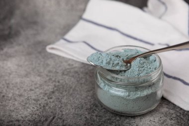 Blue spirulina powder in a glass jar on a black texture background. Natural superfood, vegan, healthy food supplement. Phycocyanin extract. Antioxidant. Place for text. Copy space.