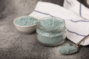 Blue spirulina powder in a glass jar on a black texture background. Natural superfood, vegan, healthy food supplement. Phycocyanin extract. Antioxidant. Place for text. Copy space.