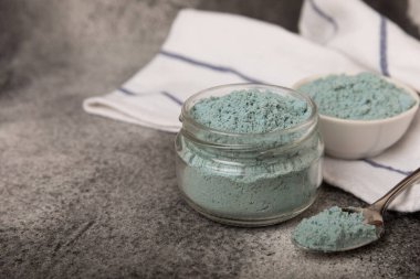 Blue spirulina powder in a glass jar on a black texture background. Natural superfood, vegan, healthy food supplement. Phycocyanin extract. Antioxidant. Place for text. Copy space.