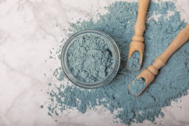 Blue spirulina powder in jars, bowls and spoons on a marble background. Natural superfood, vegan, healthy food supplement. Phycocyanin extract. Antioxidant. Place for text. Copy space.