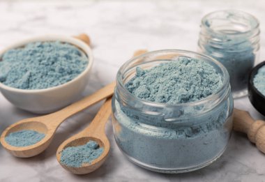 Blue spirulina powder in jars, bowls and spoons on a marble background. Natural superfood, vegan, healthy food supplement. Phycocyanin extract. Antioxidant. Place for text. Copy space.