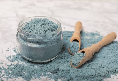 Blue spirulina powder in jars, bowls and spoons on a marble background. Natural superfood, vegan, healthy food supplement. Phycocyanin extract. Antioxidant. Place for text. Copy space.