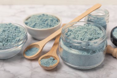 Blue spirulina powder in jars, bowls and spoons on a marble background. Natural superfood, vegan, healthy food supplement. Phycocyanin extract. Antioxidant. Place for text. Copy space.