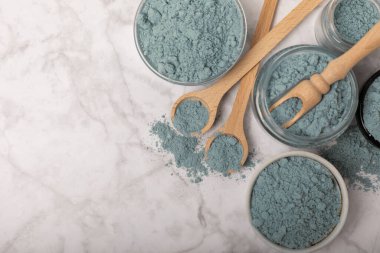 Blue spirulina powder in jars, bowls and spoons on a marble background. Natural superfood, vegan, healthy food supplement. Phycocyanin extract. Antioxidant. Place for text. Copy space.