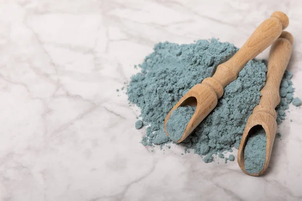 Blue spirulina powder in wooden spoons on a marble background. Natural superfood, vegan, healthy food supplement. Phycocyanin extract. Antioxidant. Place for text. Copy space.