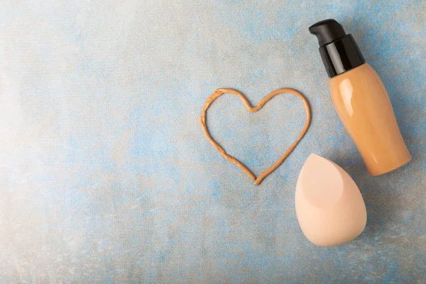 Liquid foundation for makeup and sponge blender for makeup. Foundation beauty face makeup application, perfect makeup tool. Beauty blender,bb cream or concealer on marble texture background.
