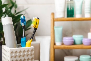 Toothbrushes and mock-up of a tube of toothpaste in a glass in the bathroom. Toothbrushes on the background of cosmetics on the shelf. Beauty concept. Dental car.