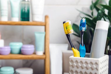 Toothbrushes and mock-up of a tube of toothpaste in a glass in the bathroom. Toothbrushes on the background of cosmetics on the shelf. Beauty concept. Dental car.