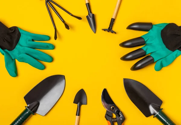 Gardening tools, pruner, gardening gloves, shovel and rake on a bright yellow background. Garden conceptual composition.Place for text. Place for copying. Top view.Gardening and hobby concept.gardening tools