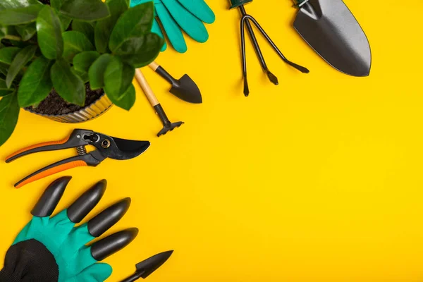 Gardening tools, pruner, gardening gloves, shovel and rake on a bright yellow background. Garden conceptual composition.Place for text. Place for copying. Top view.Gardening and hobby concept.gardening tools