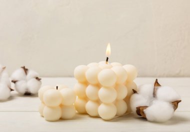 Soy wax candle on a textured table with dried cotton flowers. Interior decor with a burning handmade candle and dried flowers. Hygge home decoration concept and aromatherapy.