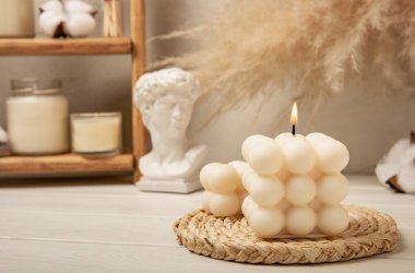 Soy wax candle on a textured table. Interior decor with a handmade burning candle. Hygge home decoration concept and aromatherapy. Bubble candle on the background of a textured wall.
