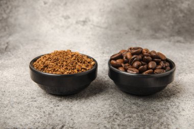 Instant coffee grains and coffee beans in bowls on a black marble background. Hot drink ingredients. Instant coffee on the table. Espresso. Place for text. Place to copy. Banner.