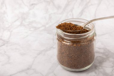 Instant coffee beans in a glass jar on a white marble background. Hot drink ingredients. Instant coffee on the table. Espresso. Place for text. Place to copy. Banner.