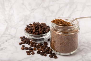Instant coffee beans in a glass jar on a white marble background. Hot drink ingredients. Instant coffee on the table. Espresso. Place for text. Place to copy. Banner.