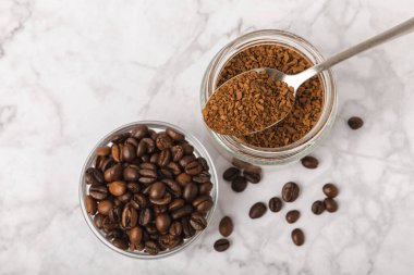 Instant coffee beans in a glass jar on a white marble background. Hot drink ingredients. Instant coffee on the table. Espresso. Place for text. Place to copy. Banner.