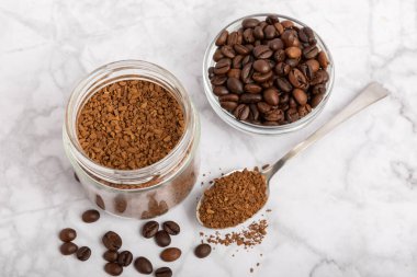 Instant coffee beans in a glass jar on a white marble background. Hot drink ingredients. Instant coffee on the table. Espresso. Place for text. Place to copy. Banner.