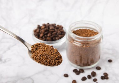 Instant coffee beans in a glass jar on a white marble background. Hot drink ingredients. Instant coffee on the table. Espresso. Place for text. Place to copy. Banner.