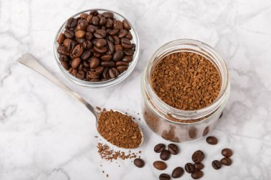 Instant coffee beans in a glass jar on a white marble background. Hot drink ingredients. Instant coffee on the table. Espresso. Place for text. Place to copy. Banner.