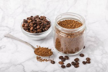 Instant coffee beans in a glass jar on a white marble background. Hot drink ingredients. Instant coffee on the table. Espresso. Place for text. Place to copy. Banner.