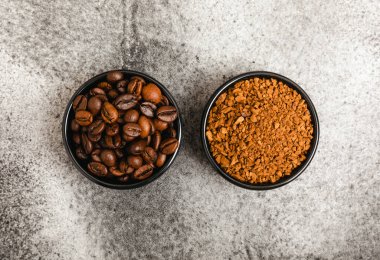 Instant coffee grains and coffee beans in bowls on a black marble background. Hot drink ingredients. Instant coffee on the table. Espresso. Place for text. Place to copy. Banner.