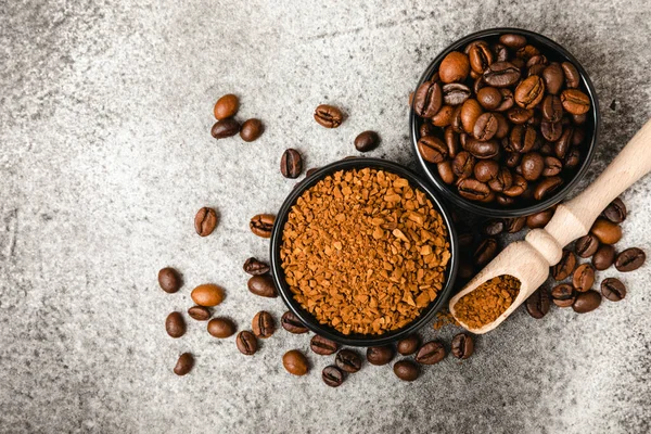 Instant coffee grains and coffee beans in bowls on a black marble background. Hot drink ingredients. Instant coffee on the table. Espresso. Place for text. Place to copy. Banner.
