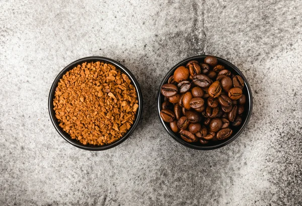 Instant coffee grains and coffee beans in bowls on a black marble background. Hot drink ingredients. Instant coffee on the table. Espresso. Place for text. Place to copy. Banner.