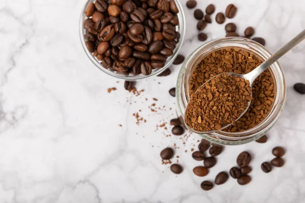Instant coffee beans in a glass jar on a white marble background. Hot drink ingredients. Instant coffee on the table. Espresso. Place for text. Place to copy. Banner.