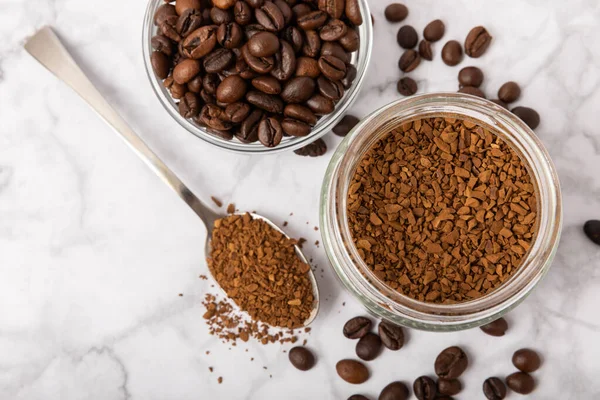 Instant coffee beans in a glass jar on a white marble background. Hot drink ingredients. Instant coffee on the table. Espresso. Place for text. Place to copy. Banner.