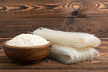 Funchoza.Dried raw rice noodles and rice on a brown wooden background.Noodles with rice flour. Diet food. Healthy food. Place for text. Place for copying.