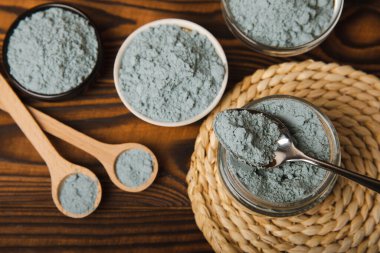 Blue spirulina powder in a bowl, jars and spoons on a brown wooden table. Natural vegan superfood. Healthy food supplement. Phycocyanin extract. Place for text. Place for a copy.