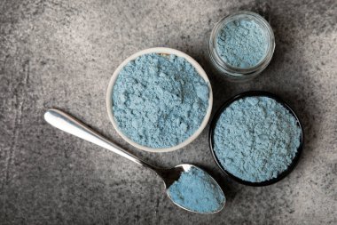Blue spirulina powder in a bowl, jars and spoons on a black textured surface. Natural vegan superfood. Healthy food supplement. Phycocyanin extract. Place for text. Place for a copy.