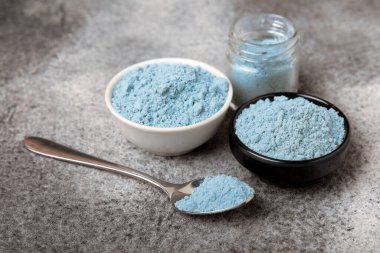 Blue spirulina powder in a bowl, jars and spoons on a black textured surface. Natural vegan superfood. Healthy food supplement. Phycocyanin extract. Place for text. Place for a copy.