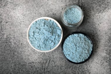 Blue spirulina powder in a bowl, jars and spoons on a black textured surface. Natural vegan superfood. Healthy food supplement. Phycocyanin extract. Place for text. Place for a copy.