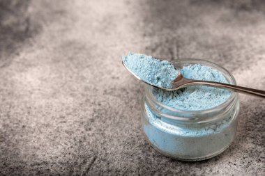 Blue spirulina powder in a bowl on a black textured surface. Natural vegan superfood. Healthy food supplement. Phycocyanin extract. Place for text. Place for a copy.
