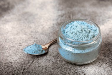 Blue spirulina powder in a bowl on a black textured surface. Natural vegan superfood. Healthy food supplement. Phycocyanin extract. Place for text. Place for a copy.