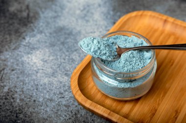 Blue spirulina powder in a bowl on a black textured surface. Natural vegan superfood. Healthy food supplement. Phycocyanin extract. Place for text. Place for a copy.