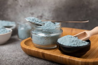 Blue spirulina powder in a bowl, jars and spoons on a black textured surface. Natural vegan superfood. Healthy food supplement. Phycocyanin extract. Place for text. Place for a copy.