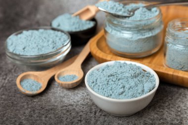 Blue spirulina powder in a bowl, jars and spoons on a black textured surface. Natural vegan superfood. Healthy food supplement. Phycocyanin extract. Place for text. Place for a copy.
