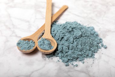 Blue spirulina powder in bowls and spoons on a marble table. Natural vegan superfood. Healthy food supplement. Phycocyanin extract. Place for text. Place for a copy.