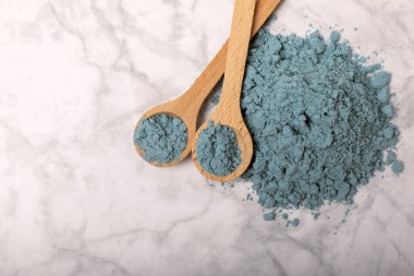Blue spirulina powder in bowls and spoons on a marble table. Natural vegan superfood. Healthy food supplement. Phycocyanin extract. Place for text. Place for a copy.